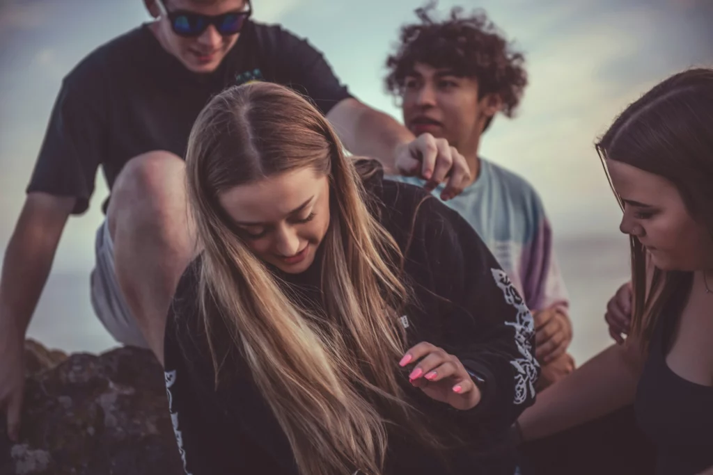Jeune fille regardant vers le bas entourée d'un groupe de jeunes, illustrant la peur du regard des autres et le sentiment d'être observé