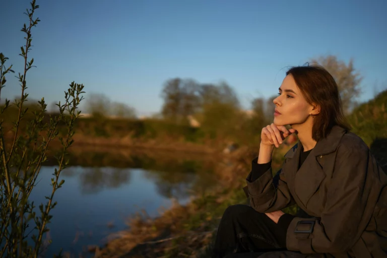Jeune femme pensive assise au bord de l'eau, regard perdu face à l'éco-anxiété
