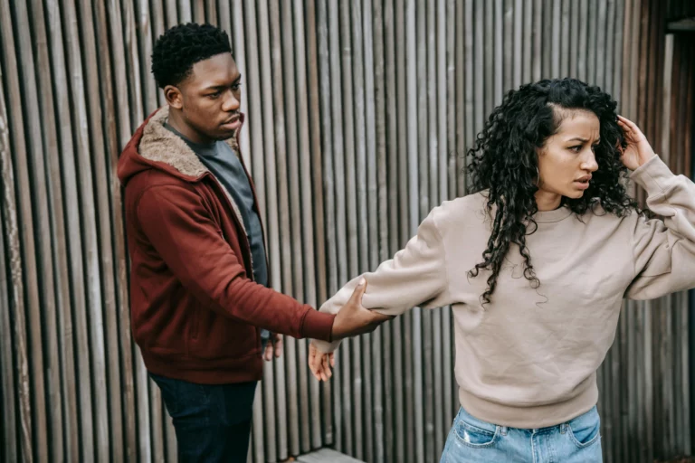 Homme retenant le bras d'une femme qui tente de partir, illustrant le contrôle et l'emprise dans une relation toxique
