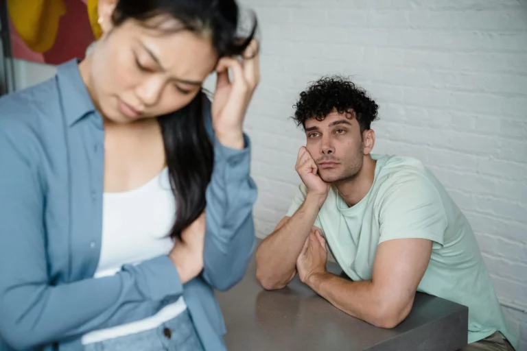 Couple assis à une table, femme la tête dans les mains et homme distant, illustrant la tension dans une relation toxique