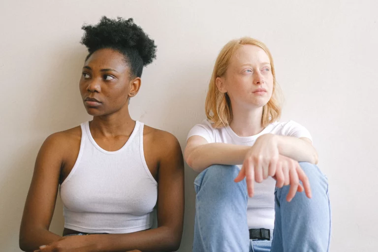 Deux jeunes femmes assises côte à côte sans se regarder, illustrant la tension d'une rupture amicale