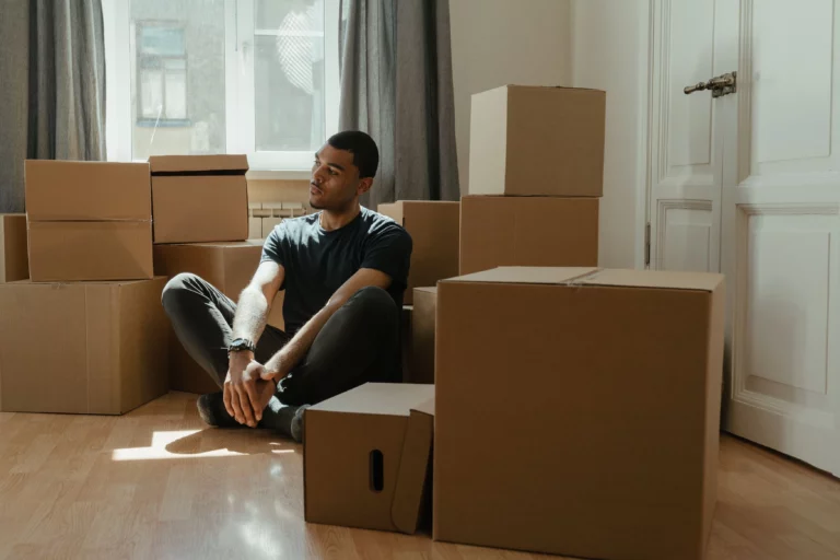 Jeune homme assis au milieu de cartons de déménagement, une image du mal du pays quand on quitte chez soi