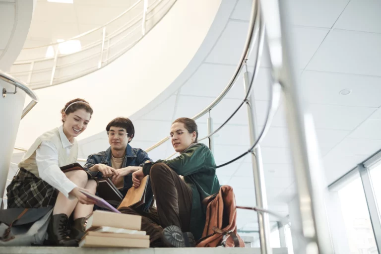 Trois étudiants discutent assis dans les escaliers de leur campus, un moment propice pour se faire des amis